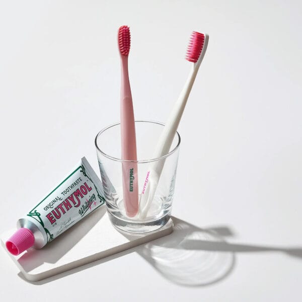 Brosse à dents Euthymol Whitening - Brosse à dents manuelle blanche avec technologie Flex-Firm pour une élimination en douceur de la plaque dentaire. Illustration brosses à dents dans un pot avec dentifrice. 