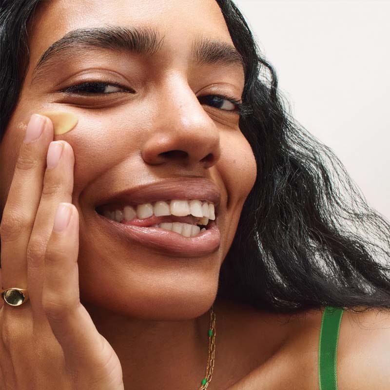 belif Super Knights Multi Vitamin Sleeping Mask 75ml Imagebild Creme offen, gelber Hintergrund – Aufhellende Nachtcreme mit Vitamin C, E, B3 & B12 für strahlende Haut am Morgen. Abbildung lachende Frau schmiert sich die Maske ins Gesicht.