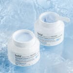 belif Cleansing Balm 100ml - Baume démaquillant hydratant à la fleur de lotus & vitamine E. Image avec applicateur, sans couvercle sur fond bleu.