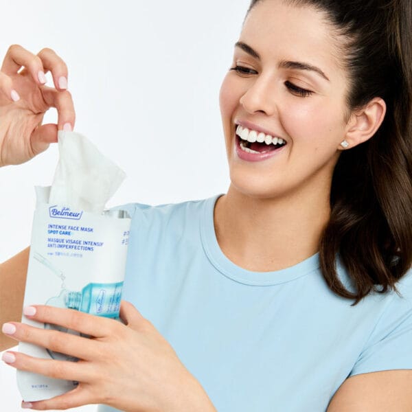 Dr. Belmeur Spot Care Intense Face Mask 30ml – beruhigende Tuchmaske mit Teebaumöl, Salicylsäure und Panthenol für unreine Haut. Abbildung Frau zieht die Maske aus der Verpackung.