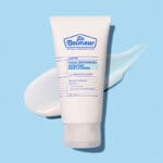 Dr. Belmeur Clarifying Facial Moisturizer 120ml – leichte Feuchtigkeitscreme für zu Akne neigende Haut mit Niacinamid und Panthenol. Abbildung Produkt mit Creme im Hintergrund.