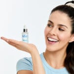 Dr. Belmeur Spot Care Ampoule 22ml – beruhigendes Serum mit Panthenol, Beta-Glucan, Chaga-Pilz und Teebaumöl gegen Unreinheiten und Rötungen. Abbildung lächelnde Frau hält das Produkt in der Hand.