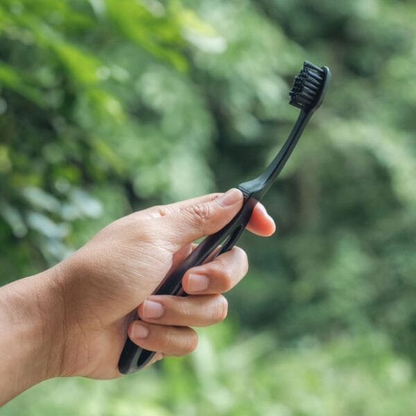 megasmile Loop toothbrush with activated carbon bristles. Picture toothbrush black in the hand, outside in the green. 