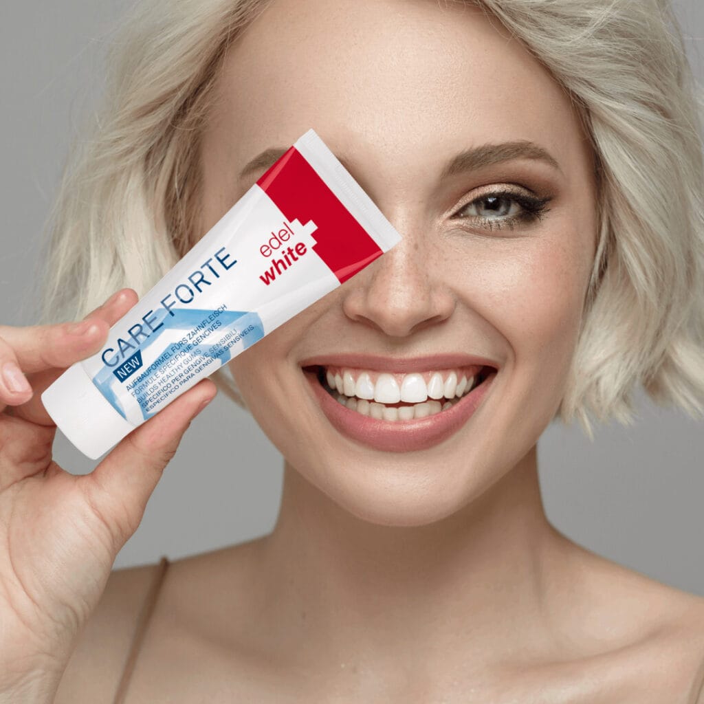Lächelnde Frau mit heller Kurzhaarfrisur hält edel+white CARE FORTE Zahngel vor ihr Auge – für gesunde, gepflegte Zähne und Zahnfleisch